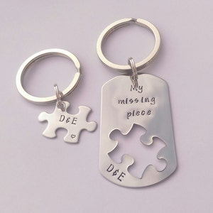 May include: Two silver keyrings with a puzzle piece design. One keyring has a puzzle piece charm with the initials "D&E" and a small heart. The other keyring has a tag with the text "My missing piece" and a cutout puzzle piece. Both keyrings have the initials "D&E" engraved on them.