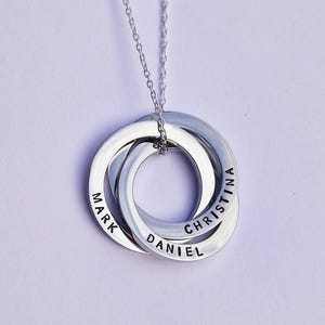 May include: Silver necklace with three interlocking rings, each engraved with a name: Mark, Daniel, and Christina.