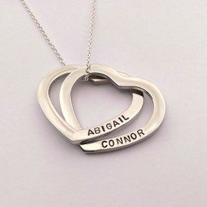 May include: Silver necklace with two interlocking heart pendants. The hearts are engraved with the names "Abigail" and "Connor".