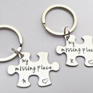 May include: Two silver puzzle piece keyrings. Each piece is engraved with "my missing piece" in a handwritten font. One keyring has the letter "M" and a heart, the other has the letter "R" and a heart.