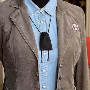 May include: A brown corduroy blazer with a blue denim shirt underneath. A black pouch hangs from a black cord around the neck.