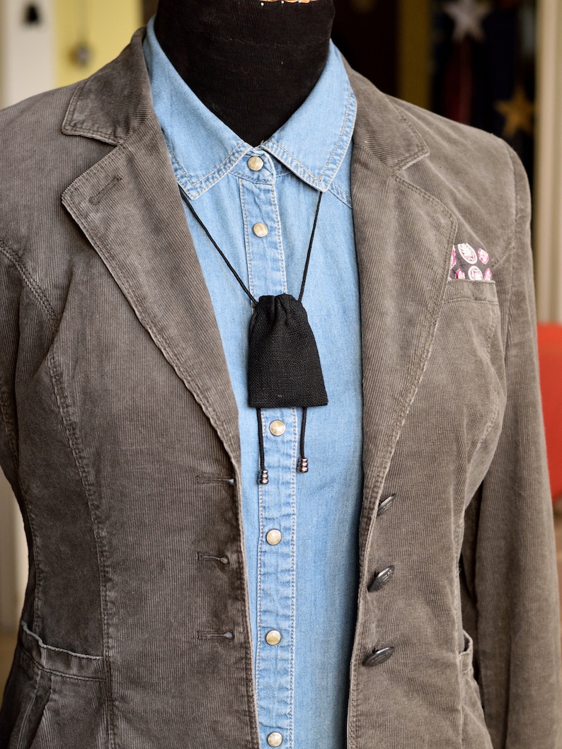 May include: A brown corduroy blazer with a blue denim shirt underneath. A black pouch hangs from a black cord around the neck.