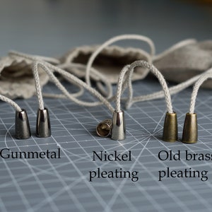 May include: Four cord ends in different finishes: gunmetal, nickel, and two old brass. The cord ends are on a gray grid surface.