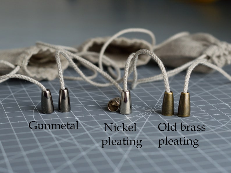 May include: Four cord ends in different finishes: gunmetal, nickel, and two old brass. The cord ends are on a gray grid surface.