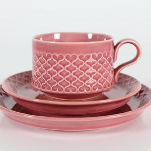 以下が含まれることがあります： ピンク色のセラミックティーカップとソーサーのセット。カップはハート型の模様とハンドルが付いています。セットには、小皿と大皿が含まれています。セットは無地のピンク色です。