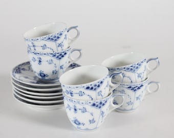 May include: A set of white porcelain teacups and saucers with a blue floral design. The teacups are stacked, and the saucers are in a neat pile. The teacups have a curved handle and a delicate, detailed pattern.