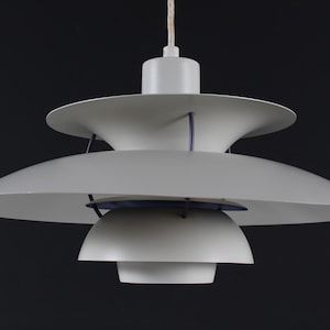 May include: A white pendant light with multiple tiers and a white cord. The light has a modern design with a layered, geometric shape.