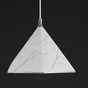 May include: White, triangular pendant light with a silver trim and a black floral design. The light hangs from a white cord against a black background. The light fixture has a modern, minimalist design.