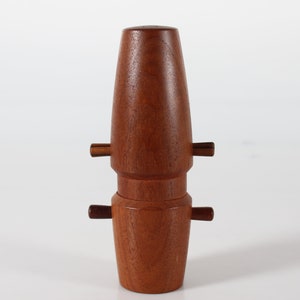 Może przedstawiać: Ręcznie wykonany drewniany korek do butelki o bogatym, czerwonobrązowym wykończeniu. Korek ma cylindryczny kształt z dwoma zestawami małych, poziomych uchwytów. Całkowity kształt przypomina stylizowaną klepsydrę.