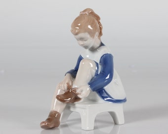 Royal Copenhagen Figurine of a Girl Tying her Shoes made by Bing & Grøndahl Model No. 2373 by Danish Artist Claire Weiss. Mid-century