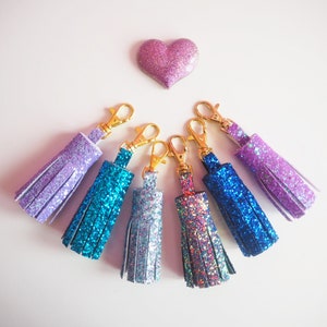 May include: Six sparkly keychains with gold clasps. The keychains are in shades of purple, blue, and teal.
