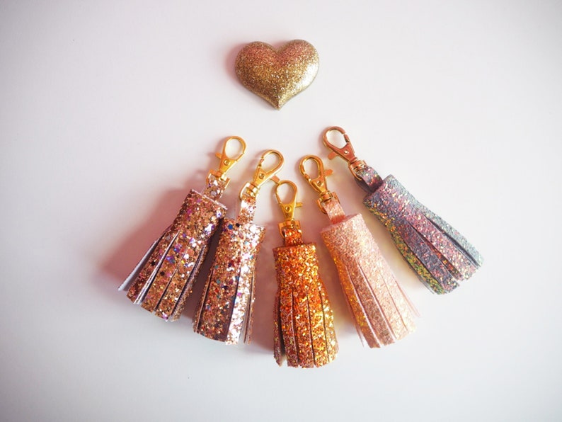 May include: Five sparkly keychains with gold-tone metal rings. The keychains are made of faux leather and have a tassel design. The tassels are in shades of pink, gold, orange, and blue.