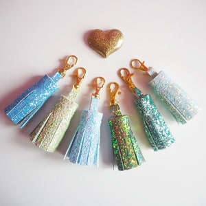 May include: Seven sparkly tassel keychains in various shades of blue, green, and iridescent colours. Each keychain has a gold metal clasp.