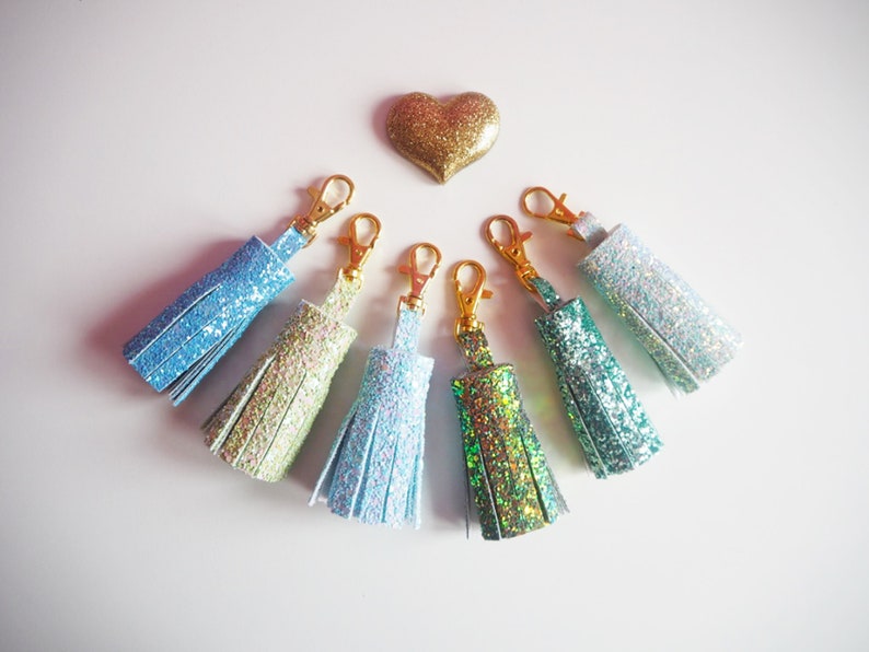 May include: Seven sparkly tassel keychains in various shades of blue, green, and iridescent colours. Each keychain has a gold metal clasp.