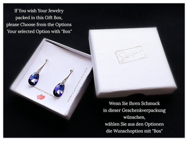 Pu&ograve; includere: Una scatola regalo bianca con un paio di orecchini a goccia viola all'interno. La scatola ha il testo "If You wish Your Jewelry packed in this Gift Box, please Choose from the Options Your selected Option with "Box"" in alto e il testo "Wenn Sie Ihren Schmuck in dieser Geschenkverpackung w&uuml;nschen, w&auml;hlen Sie aus den Optionen die Wunschoption mit "Box"" in basso.