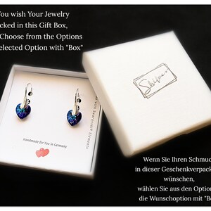 May include: A white gift box with a pair of silver heart-shaped earrings with blue and purple crystals. The box has the text "If You wish Your Jewelry packed in this Gift Box, please Choose from the Options Your selected Option with "Box" Handmade for You in Germany" printed on it. The box also has the text "Shiyoun" printed on it.