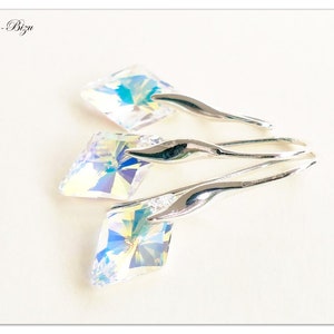 May include: Three silver dangle earrings with iridescent crystal stones. The stones are square shaped and have a faceted design. The earrings are a simple and elegant design.