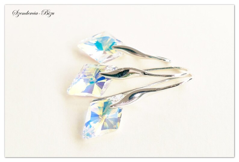 May include: Three silver dangle earrings with iridescent crystal stones. The stones are square shaped and have a faceted design. The earrings are a simple and elegant design.