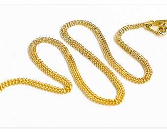 May include: A gold-colored chain necklace with a textured, woven design. The necklace is displayed on a white background, with a clasp at one end. The chain is approximately 18 inches long.