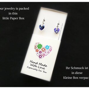 May include: A small white box with a heart design made of colorful flowers. The box has text that reads "Hand Made With Love Especially For You". The box also has text in German that reads "Ihr Schmuck ist in diese Kleine Box verpackt".