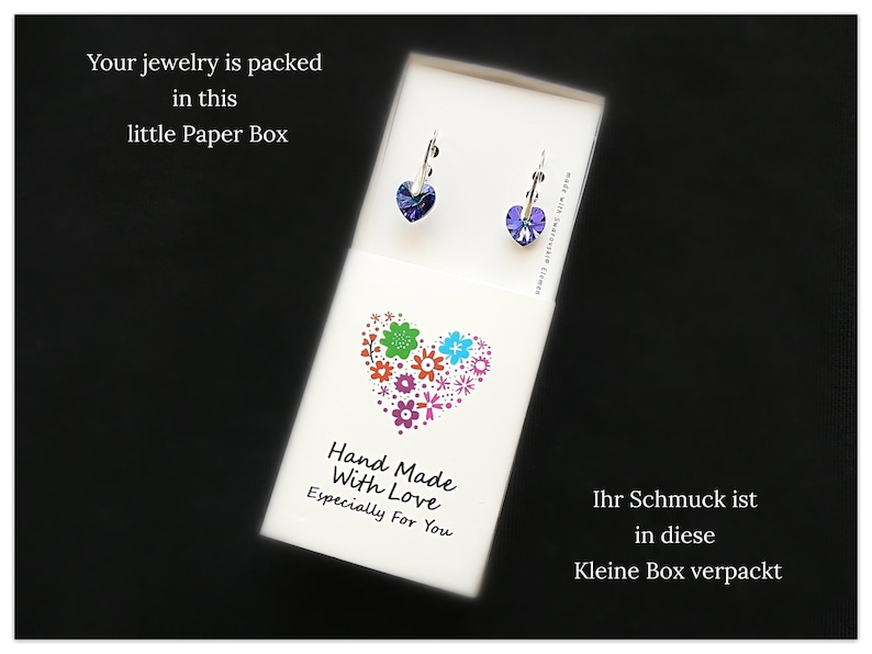 May include: A small white box with a heart design made of colorful flowers. The box has text that reads "Hand Made With Love Especially For You". The box also has text in German that reads "Ihr Schmuck ist in diese Kleine Box verpackt".