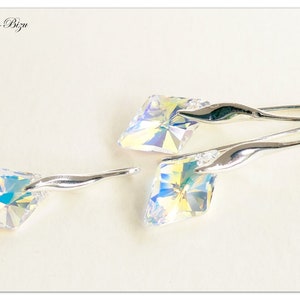 May include: A pair of silver earrings with iridescent crystal stones. The earrings have a curved, wave-like design.
