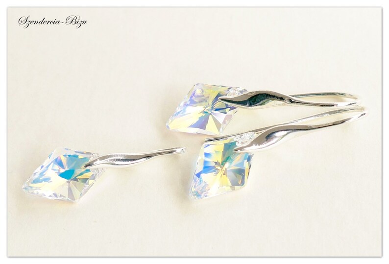 May include: A pair of silver earrings with iridescent crystal stones. The earrings have a curved, wave-like design.