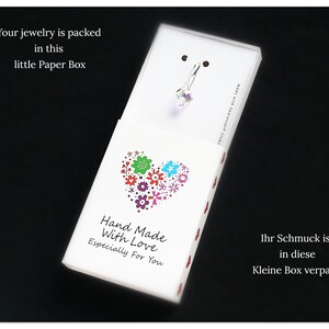 May include: A white paper box with a red dotted border. The box has a heart-shaped design with colorful flowers inside. The text on the box reads "Hand Made With Love Especially For You".