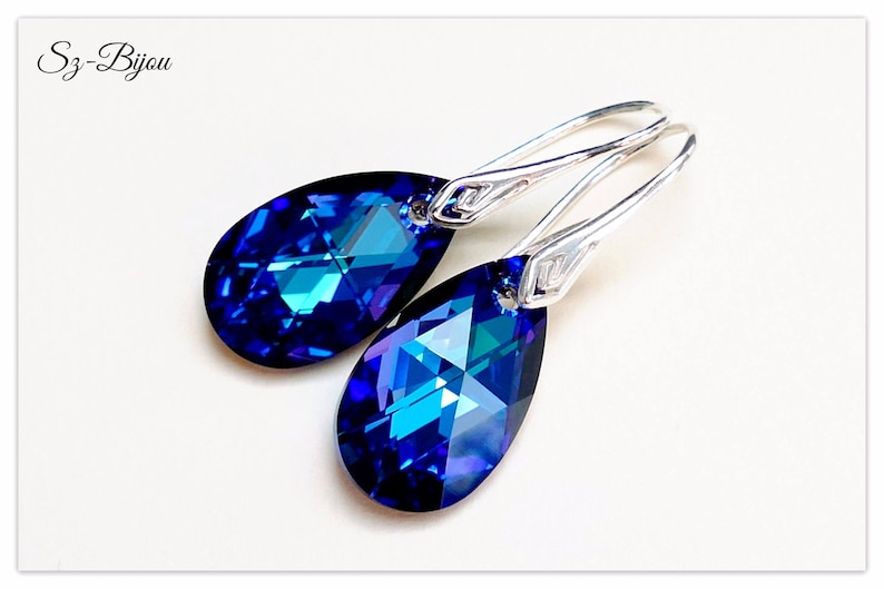 Pu&ograve; includere: Un paio di orecchini pendenti in argento con pietre di cristallo blu a forma di goccia. I cristalli hanno un design sfaccettato e brillano alla luce.