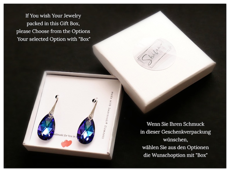 Pu&ograve; includere: Un paio di orecchini a forma di goccia con accenti di cristallo blu e viola. Gli orecchini sono confezionati in una scatola regalo bianca con il testo "Shiver" sulla parte superiore. Il testo "If You wish Your Jewelry packed in this Gift Box, please Choose from the Options Your selected Option with "Box"" &egrave; visibile nell'angolo in alto a sinistra dell'immagine.