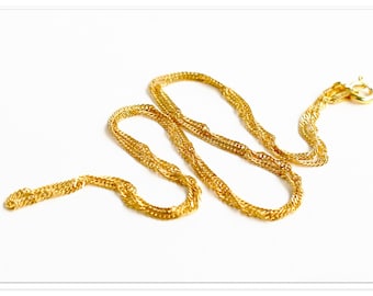 May include: A gold-colored necklace with a twisted rope design. The necklace is lying on a white surface. The clasp is visible at the end of the necklace.
