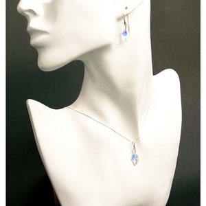 May include: A silver necklace and earrings set with a clear crystal pendant and matching earrings. The jewelry is displayed on a white mannequin bust.