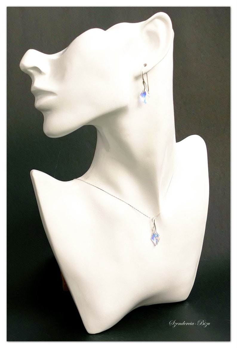May include: A silver necklace and earrings set with a clear crystal pendant and matching earrings. The jewelry is displayed on a white mannequin bust.