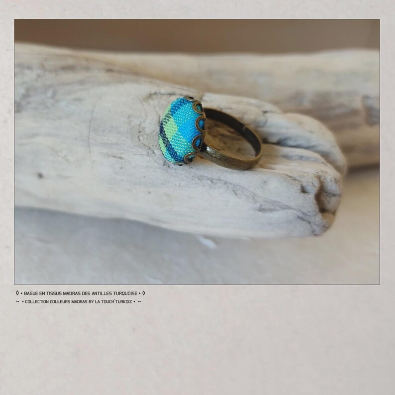 Puede incluir: Un anillo artesanal con un dise&ntilde;o de tela turquesa y azul. El anillo tiene una banda de color bronce y un bisel decorativo. El texto de la imagen dice "BAGUES EN TISSUS MADRAS DES ANTILLES TURQUOISE" y "COLLECTION COULEURS MADRAS BY LA TOUCH TURKOIZ."