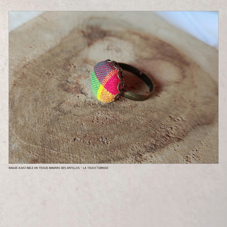 Puede incluir: Anillo ajustable con un dise&ntilde;o de tela colorida. El anillo presenta una pieza central redonda de tela multicolor en tonos de rojo, amarillo, verde y rosa, engastada en un marco de metal color bronce. El anillo se muestra sobre una superficie de madera.