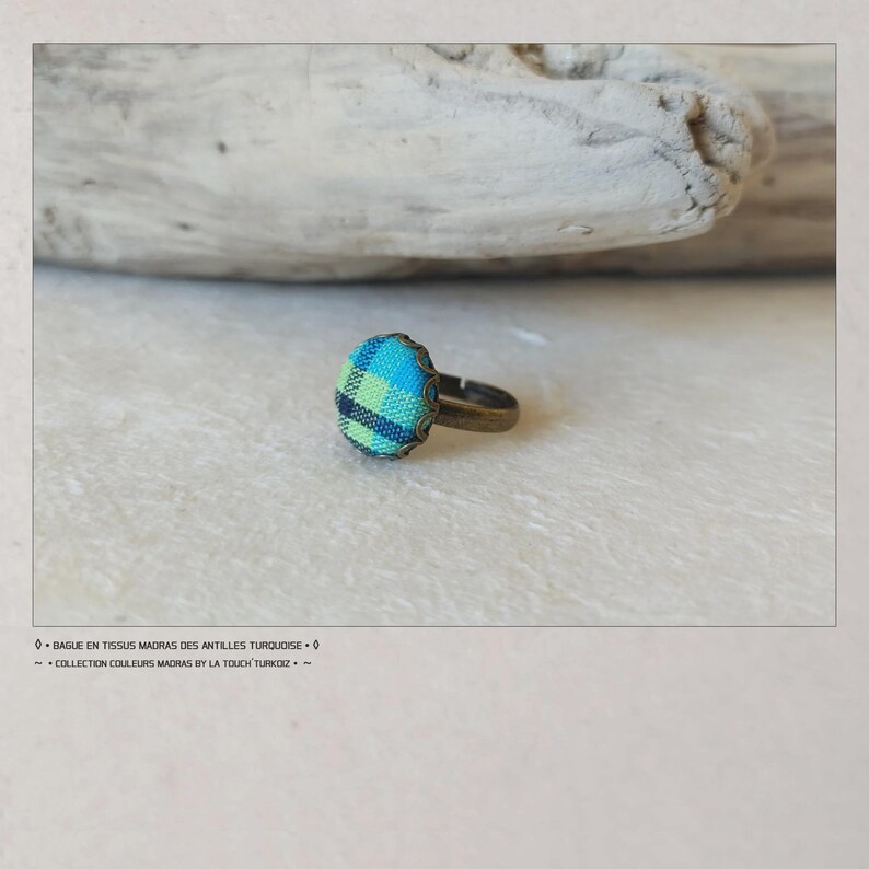 Puede incluir: Un anillo con un centro de tela a cuadros turquesa, azul y verde. El anillo tiene una banda de color bronce. El texto de la imagen dice "BAGUES EN TISSUS MADRAS DES ANTILLES TURQUOISE" y "COLLECTION COULEURS MADRAS BY LA TOUCH TURKOIZ."