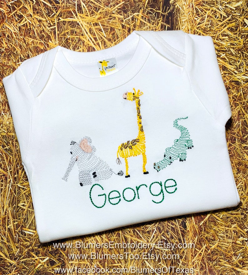 May include: A white short-sleeved baby bodysuit featuring an embroidered design of a gray elephant, a yellow giraffe, and a green alligator. Below the animals, the name George is embroidered in green thread. A small giraffe logo tag is at the neck.