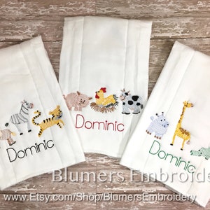 May include: Three white burp cloths featuring embroidered animal designs and the name Dominic. The left cloth shows a lion, zebra, and tiger. The center cloth displays a pig, rooster, and cow. The right cloth features a hippo, giraffe, and alligator.