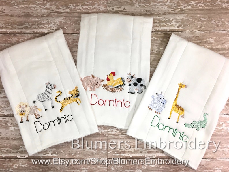 May include: Three white burp cloths featuring embroidered animal designs and the name Dominic. The left cloth shows a lion, zebra, and tiger. The center cloth displays a pig, rooster, and cow. The right cloth features a hippo, giraffe, and alligator.
