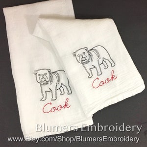 Monogrammed Bulldog Kitchen Dish Towel Personalized Dog Gift Custom Pet Flour Sack Tea Towel  Hostess Gift Personalized Bulldog Gift: Two white kitchen towels with black embroidered bulldog illustrations and the word 'Cook' in red embroidery. The towels are folded and displayed on a black background. The text 'Blumers Embroidery' and 'www.Etsy.com/Shop/BlumersEmbroidery' is visible at the bottom of the image.