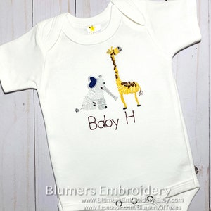 May include: A white short-sleeved baby bodysuit featuring an embroidered gray elephant and a yellow giraffe. Below the animals, the text Baby H is embroidered in black thread. The garment has a round neckline and three metal snaps at the bottom.