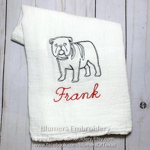 K&ouml;nnte beinhalten: Ein wei&szlig;es K&uuml;chentuch mit einer schwarzen Stickerei, die den Umriss einer Bulldogge zeigt, sowie dem Namen Frank in rotem Schreibschriftgarn. Das Tuch hat eine strukturierte Stoffoberfl&auml;che und enth&auml;lt den Text Blumers Embroidery.