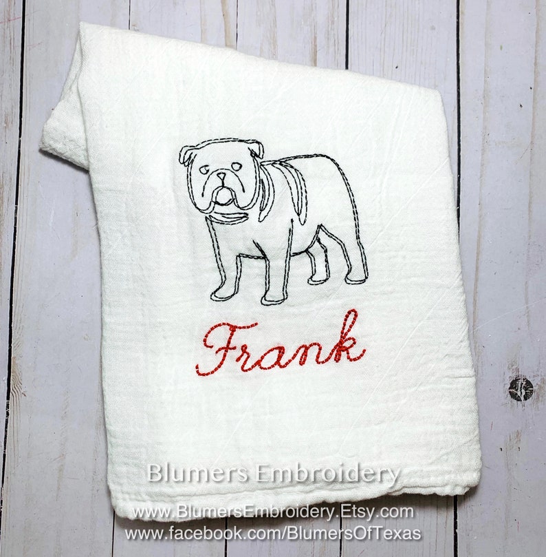 K&ouml;nnte beinhalten: Ein wei&szlig;es K&uuml;chentuch mit einer schwarzen Stickerei, die den Umriss einer Bulldogge zeigt, sowie dem Namen Frank in rotem Schreibschriftgarn. Das Tuch hat eine strukturierte Stoffoberfl&auml;che und enth&auml;lt den Text Blumers Embroidery.