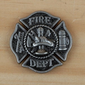 May include: A silver metal fire department badge with a Maltese cross design. The badge features a fire helmet, axe, ladder, and fire hydrant. The words "FIRE DEPT" are inscribed on the badge.