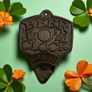 May include: A cast iron bottle opener with the words "BEER O'CLOCK" and "OPEN HERE" embossed on it. The opener is dark brown and has a textured surface. The background is light green with orange flowers and green leaves.