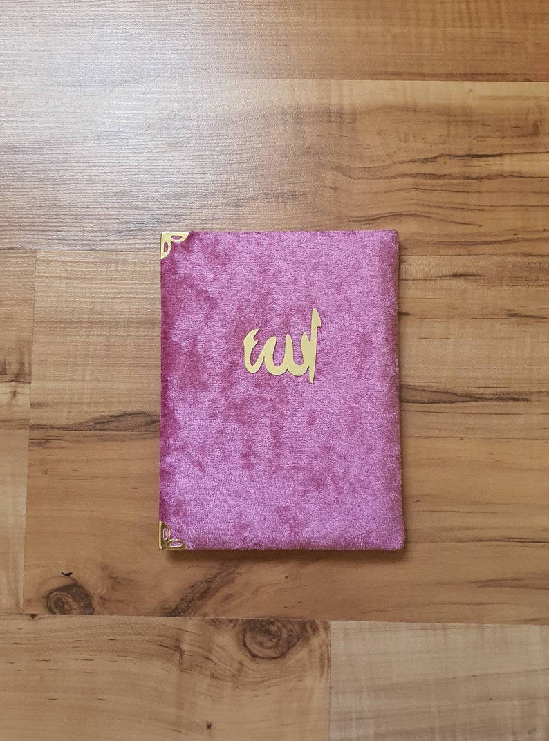 May include: A pink velvet book cover with gold corners and the word "الله" in gold lettering.