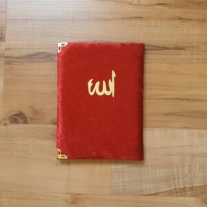 May include: A red velvet book cover with gold corners and the word "الله" in gold lettering.