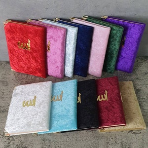 May include: A collection of 12 velvet-covered notebooks with gold lettering. The notebooks are in various colors, including red, pink, blue, green, purple, white, and turquoise. The notebooks feature the Arabic word for "God" in gold lettering.