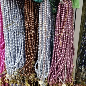 May include: A display of colorful prayer beads with tassels. The beads are made of various materials, including pearls and glass. The tassels are made of different colors and textures.