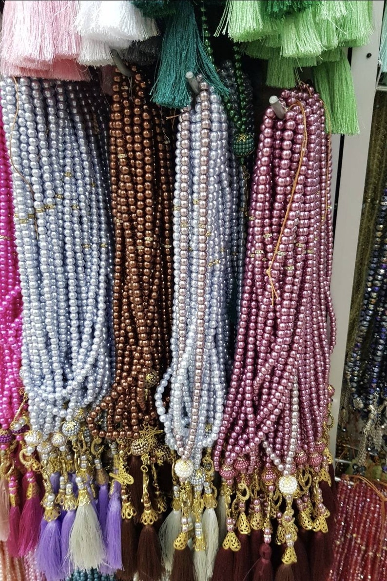 May include: A display of colorful prayer beads with tassels. The beads are made of various materials, including pearls and glass. The tassels are made of different colors and textures.